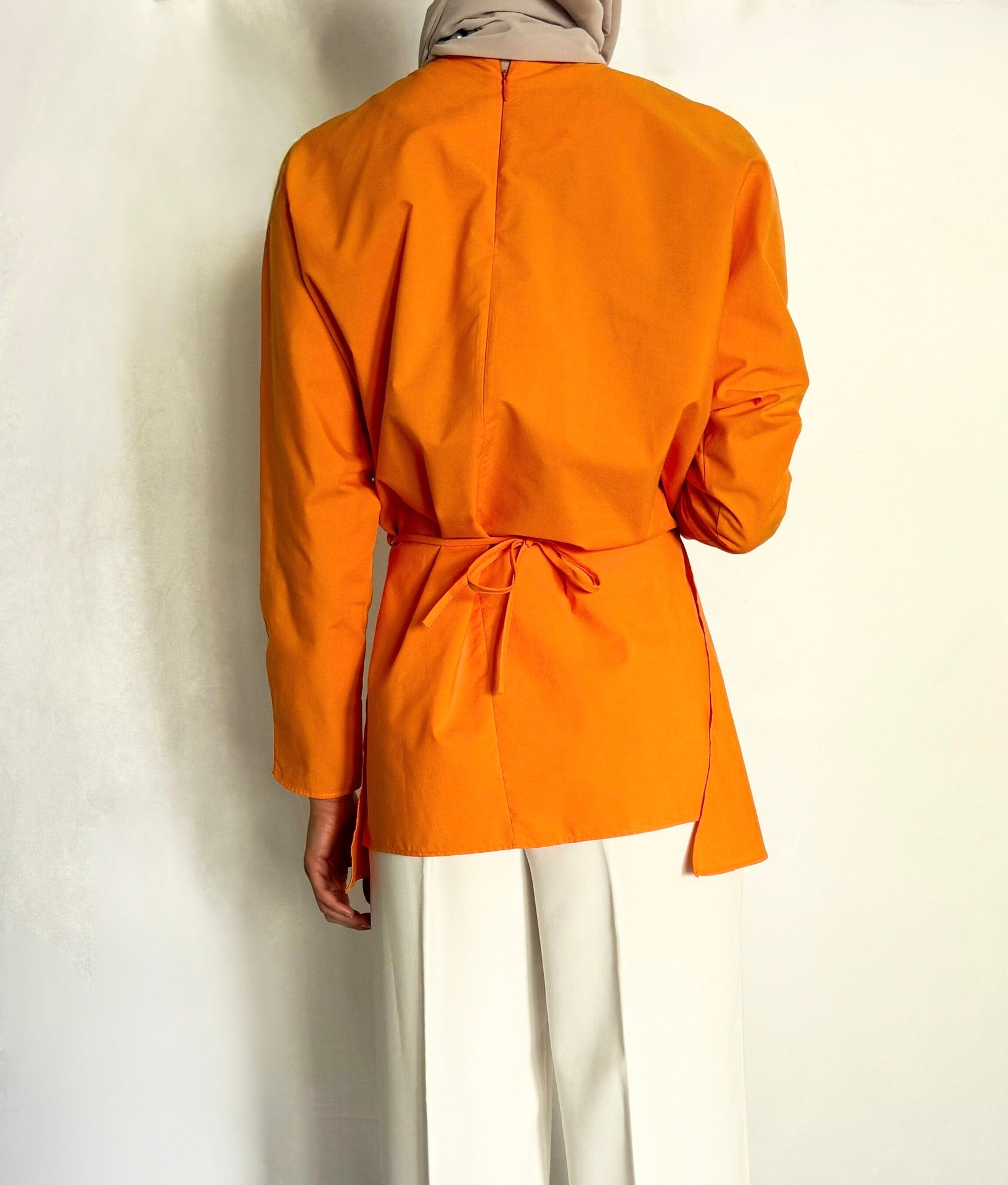 The back of an orange tunic with waist tie wrap. 