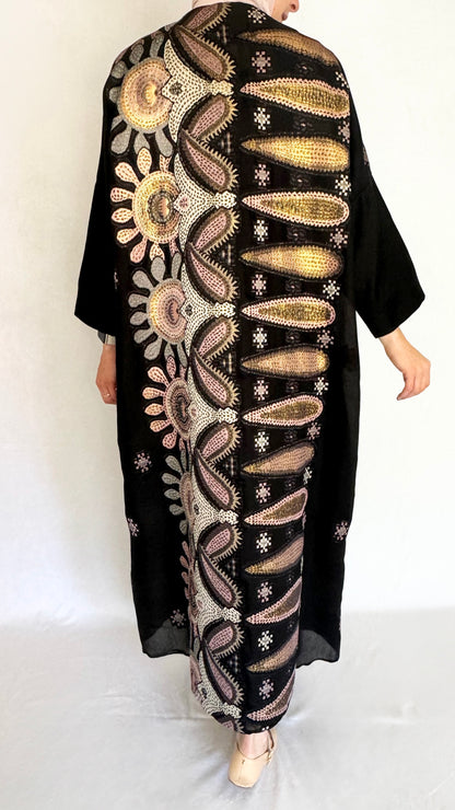 Back view of the back of the black abaya. The back has a colorful pattern design in pink and gold.